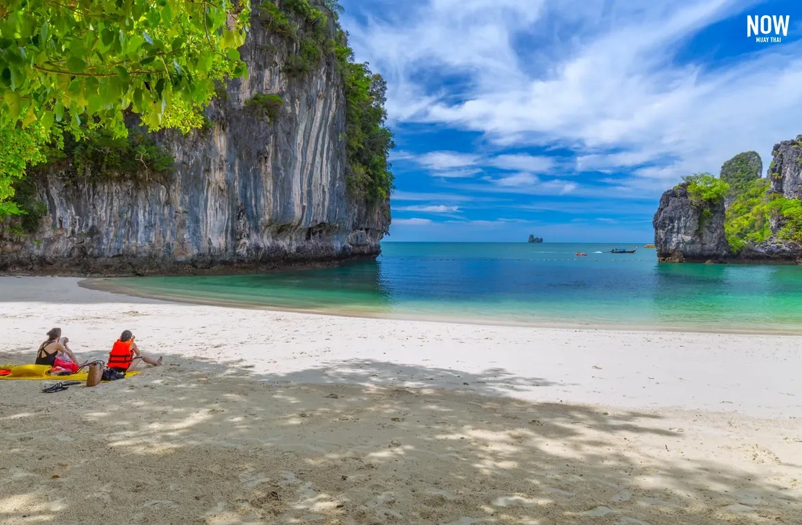 Tourists relaxing on the beach with a scenic view of turquoise sea and limestone cliffs at Koh Hong, Krabi, Thailand.
